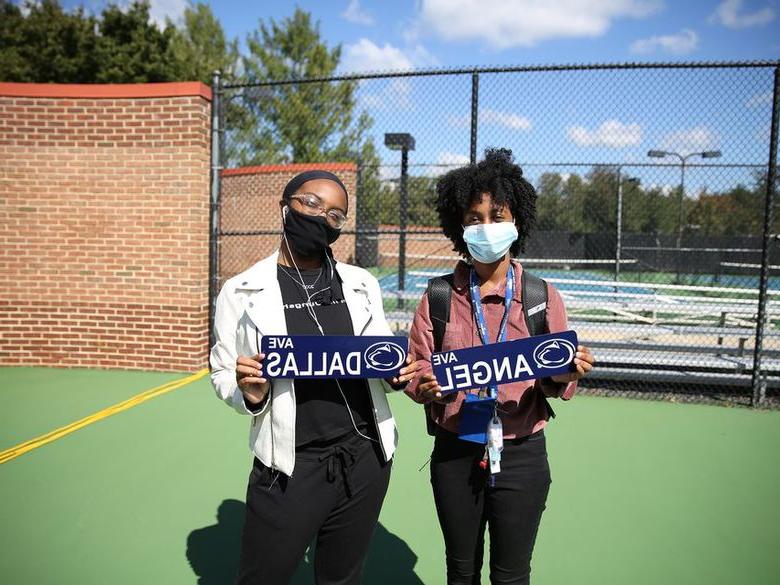 两名女学生戴着面具，举着写有自己名字的牌子.