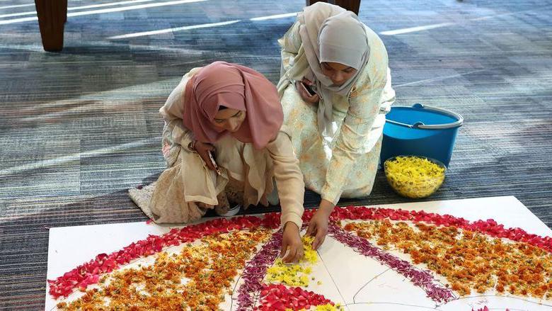两名女学生将花瓣放在地板上，做成了一个rangoli.