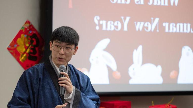 一名穿着中国传统长袍的男学生站在讲台上.